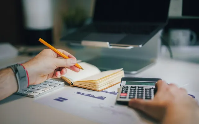 A desk with a calculator, notebook and laptop